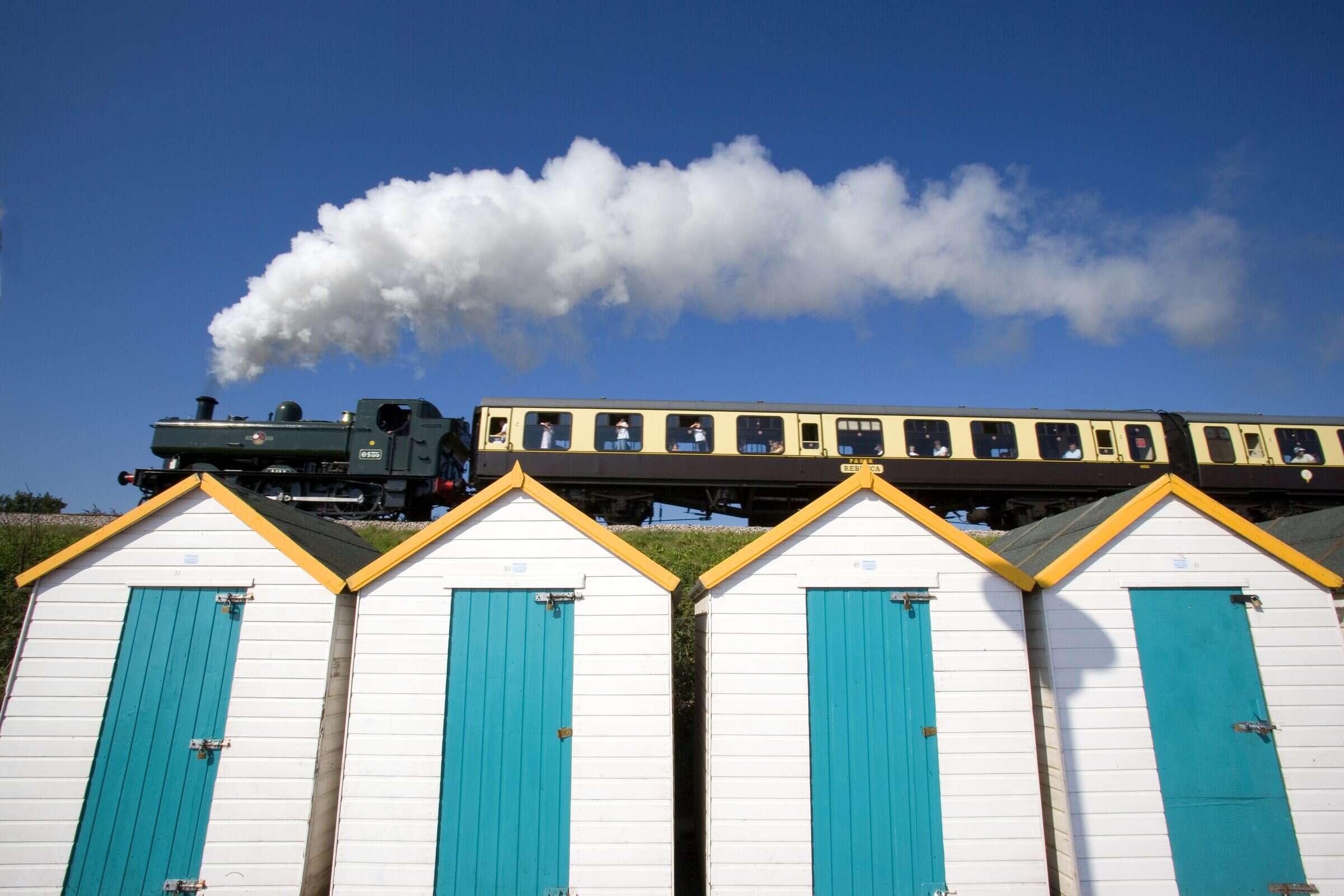 A steam train passing above a row of colourful beach huts on the English Riviera coast